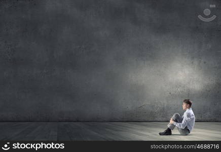 Businessman in isolation. Young depressed businessman sitting on floor alone in empty room