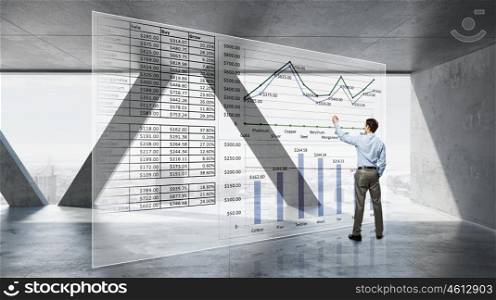 Businessman in modern interior. Back view of businessman in modern room drawing infographs on virtual panel