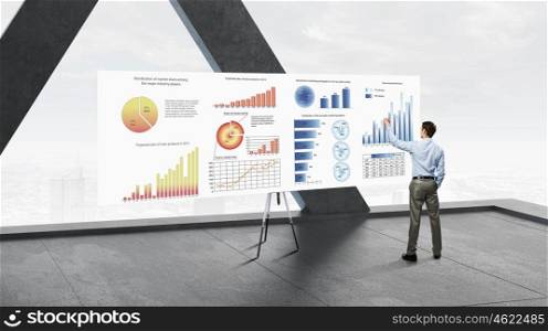Businessman in modern interior. Back view of businessman in modern room drawing infographs on banner