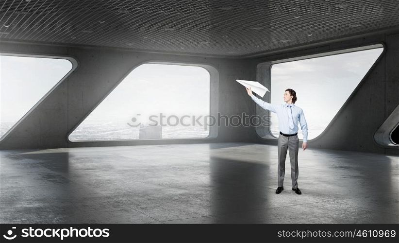 Businessman in modern interior. Businessman in top floor of modern building against window with paper airplane in hand
