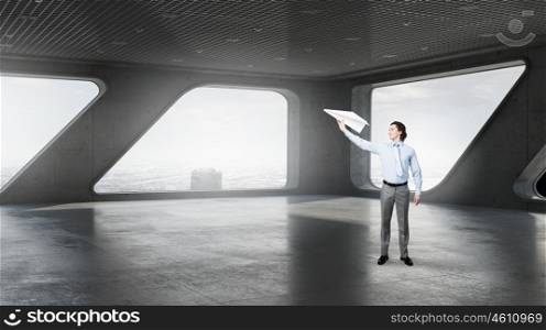Businessman in modern interior. Businessman in top floor of modern building against window with paper airplane in hand