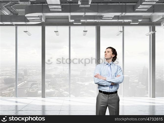 Businessman in modern interior. Confident businessman standing with arms crossed on chest in modern office