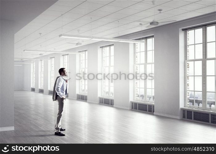 Businessman in modern office mixed media. Young elegant businessman in office looking in window