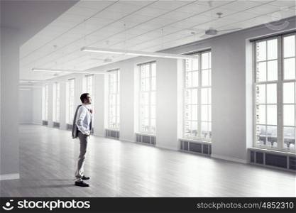 Businessman in modern office mixed media. Young elegant businessman in office looking in window