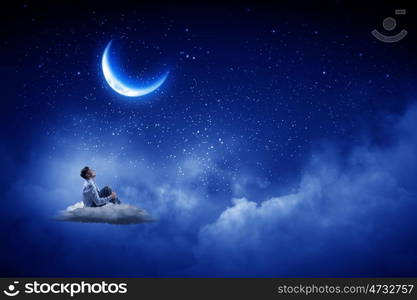 Businessman in night sky. Businessman in suit sitting on cloud in isolation and looking at moon