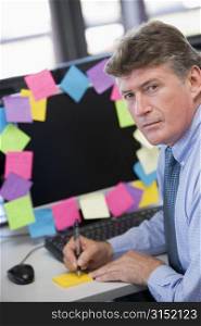 Businessman in office at monitor with notes on it writing