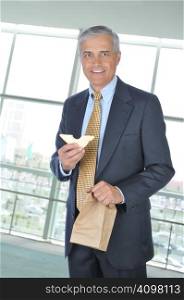 Businessman in office building holding brown bag and sandwich