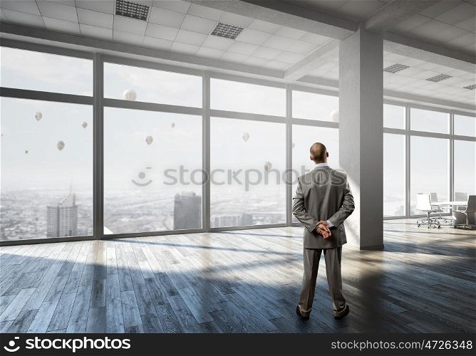 Businessman in office interior. Thoughtful businessman standing with back in empty office