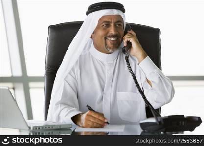 Businessman in office on telephone by laptop smiling (high key/selective focus)