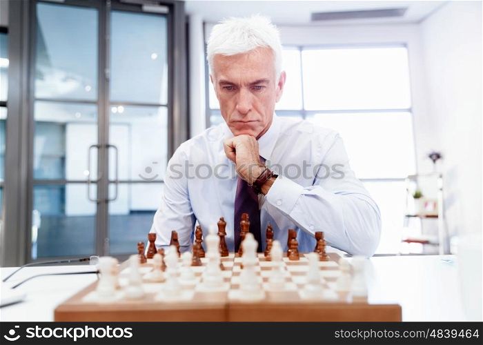 Businessman in office playing chess. Thinking the next move