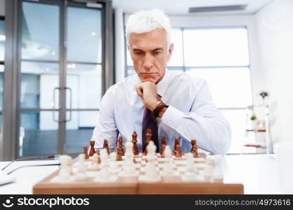 Businessman in office playing chess. Thinking the next move