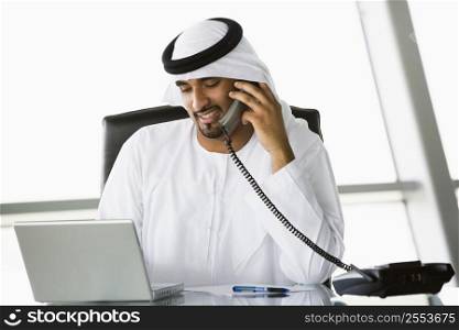 Businessman in office with laptop on telephone smiling (high key/selective focus)