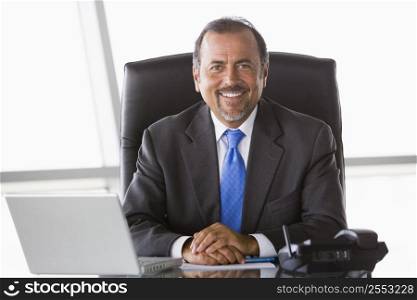 Businessman in office with laptop smiling (high key/selective focus)