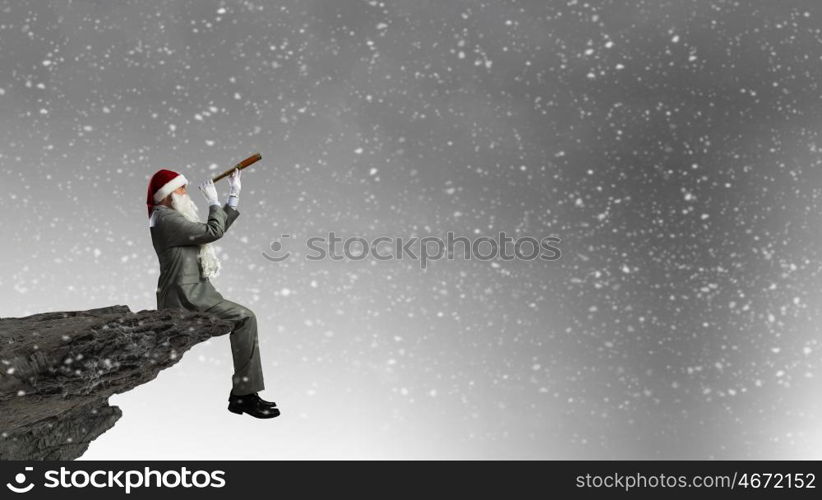 Businessman in Santa hat sitting on edge and looking in spyglass