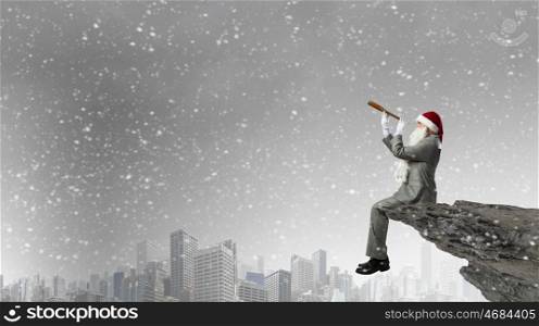 Businessman in Santa hat sitting on edge and looking in spyglass