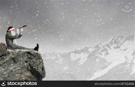 Businessman in Santa hat sitting on edge and looking in spyglass
