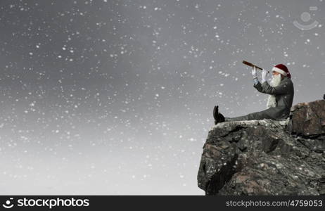 Businessman in Santa hat sitting on edge and looking in spyglass