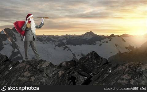 Businessman in Santa hat standing on top and looking in spyglass