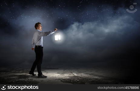 Businessman in search in darkness. Young businessman walking with lantern in darkness