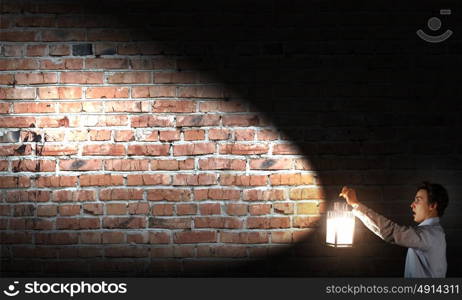 Businessman in search in darkness. Young businessman walking with lantern in darkness