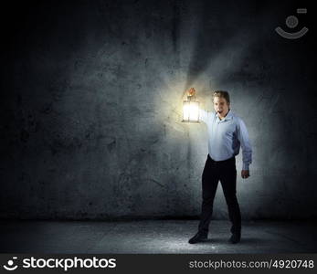 Businessman in search in darkness. Young businessman walking with lantern in darkness