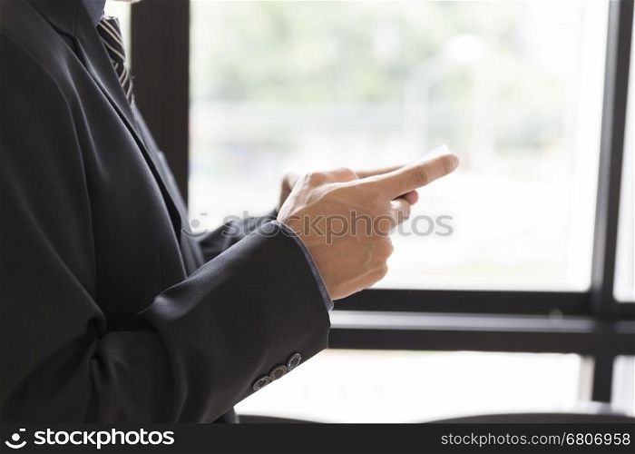 businessman in suit holding smartphone beside window