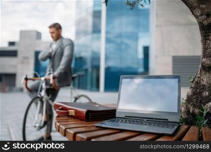 Businessman in suit on bike in downtown, glass building on background. Business person riding on eco transport on city street