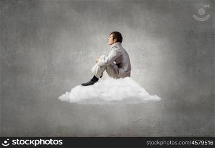 Businessman in suit sitting on cloud in isolation. Taking break from office