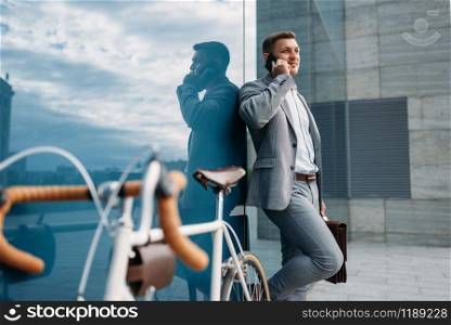 Businessman in suit talking by mobile phone at the bicycle in downtown. Business person riding on eco transport on the street. Businessman talking by mobile phone at the bicycle