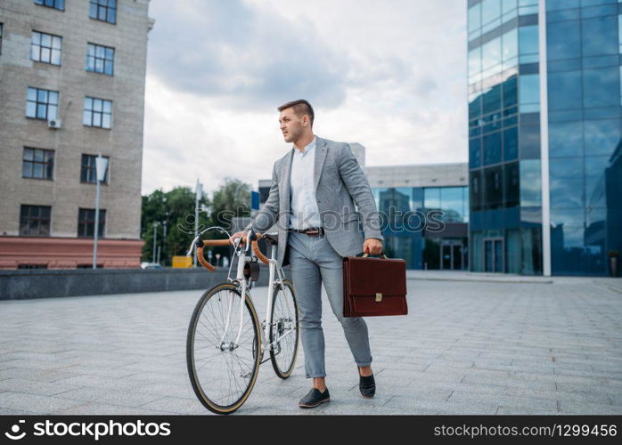 Businessman in suit with briefcase and bicycle in downtown. Business person riding on eco transport on city street