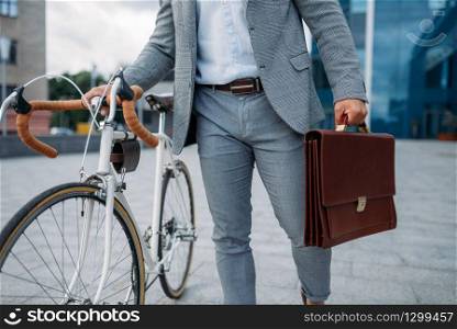 Businessman in suit with briefcase and bicycle in downtown closeup. Business person riding on eco transport on city street. Businessman with briefcase and bicycle in downtown
