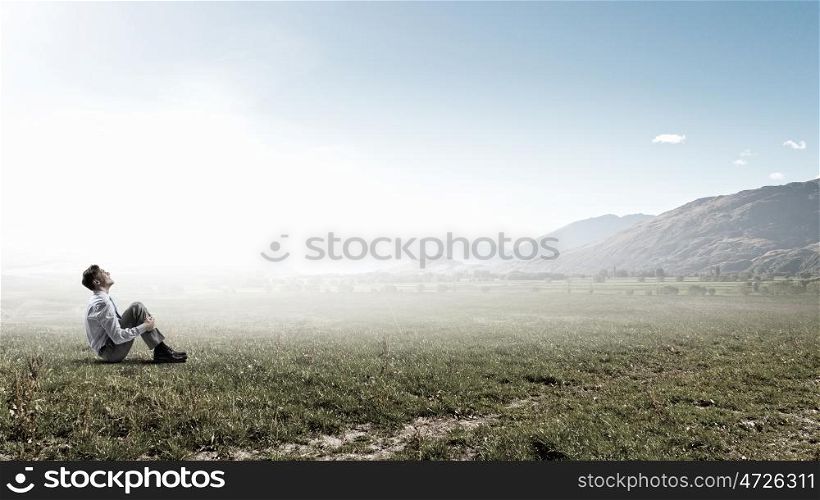 Businessman in summer park. Young businessman sitting alone on grass in park