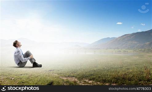 Businessman in summer park. Young businessman sitting alone on grass in park