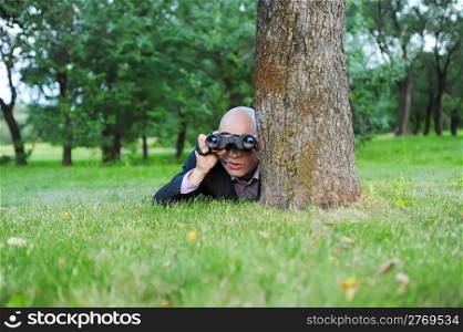 Businessman in the green park looking through binoculars