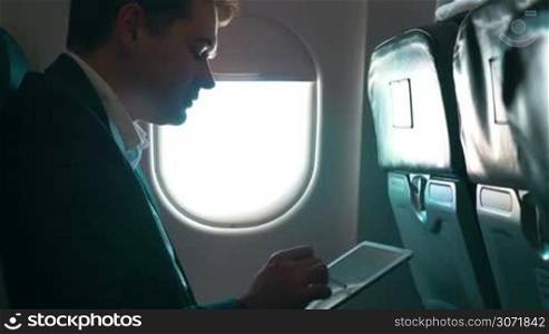 Businessman in the plane working with tablet computer. Easy work with modern devices during the trip
