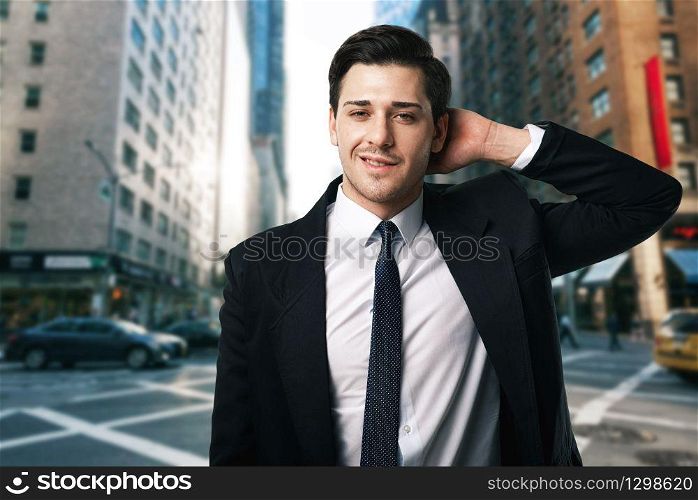 Businessman in tie and black suit poses on the street, business center on background