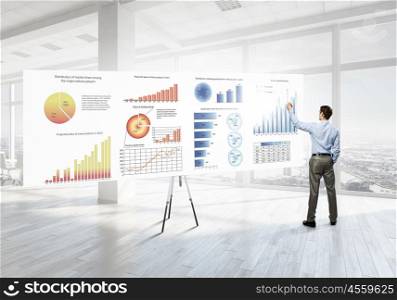 Businessman in top level office. Back view of elegant businessman against modern ofiice window drawing infographs