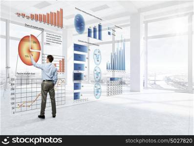 Businessman in top level office. Back view of elegant businessman against modern ofiice window drawing infographs