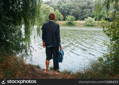 Businessman in torn suit holds briefcase on desert island, back view. Business risk, collapse or bankruptcy concept