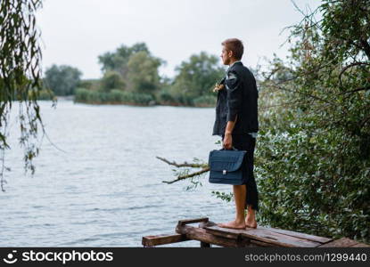 Businessman in torn suit holds briefcase on desert island, back view. Business risk, collapse or bankruptcy concept. Businessman in torn suit on desert island