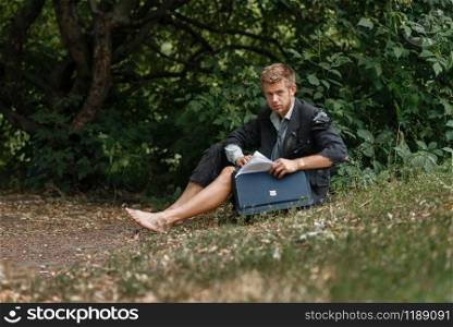Businessman in torn suit sitting on the ground on desert island. Business risk, collapse or bankruptcy concept. Businessman sitting on the ground on desert island