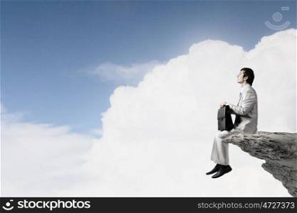 Businessman in white suit sitting on rock top. Taking break from office