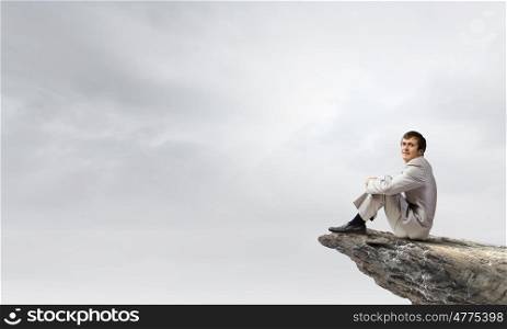 Businessman in white suit sitting on rock top. Taking break from office