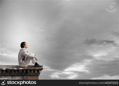 Businessman in white suit sitting on roof top. Taking break from office