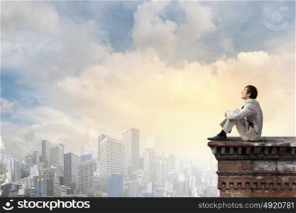 Businessman in white suit sitting on roof top. Taking break from office