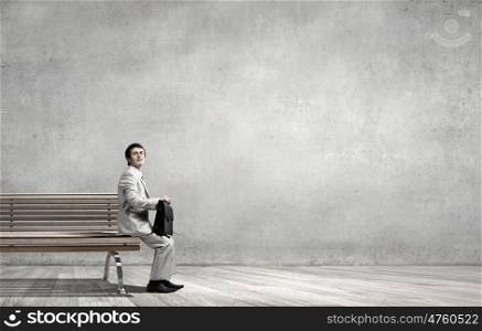 Businessman in white suit with briefcase sitting on bench. Taking break from office