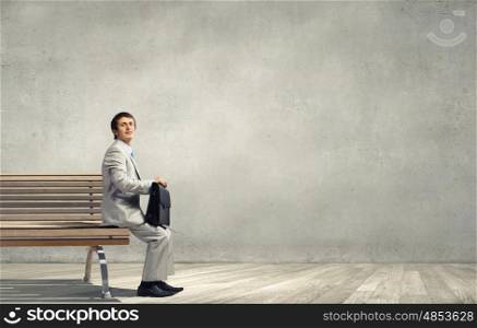 Businessman in white suit with briefcase sitting on bench. Taking break from office