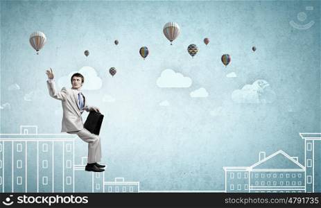 Businessman in white suit with briefcase sitting on building top. Taking break from office