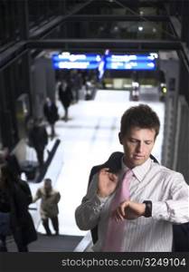 Businessman is standing on the escalator on a railwaystation or airport. He is checking the time on on his watch.