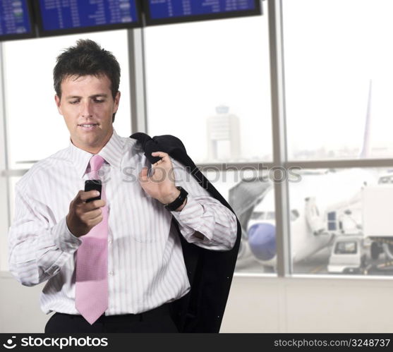 Businessman is waiting for his flight on the airport. He is playing a game or dialing someone on his mobile.